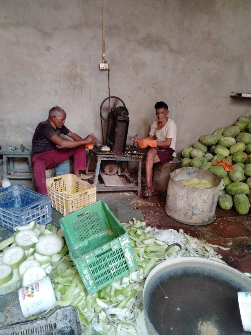 Workers seated inside a traditional petha workshop surrounded by ash gourds and processing equipment