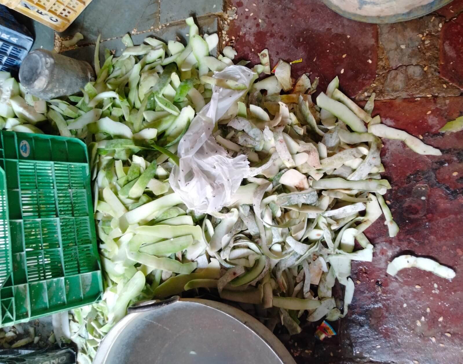 Worker preparing ash gourds beside a large pile of discarded peel
