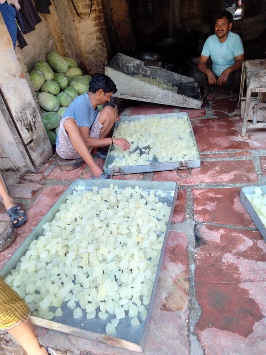 Workers sorting processed petha pieces spread across large metal trays